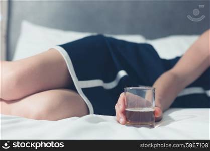 An elegant young woman is lying on a bed with a glass in her hand containing some kind of alcoholic beverage