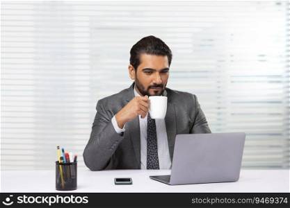 An employee holding coffee mug working on laptop in his office.