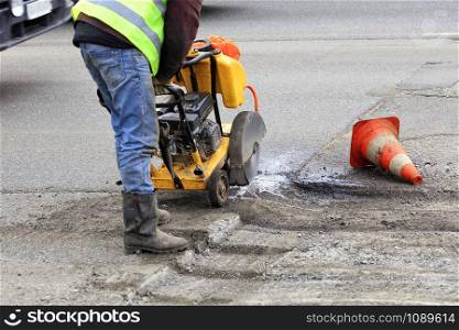An employee of the road maintenance service removes old asphalt with a gasoline carver during repairs on the carriageway.. Worker cuts a piece of bad asphalt with a gasoline cutter during road construction.