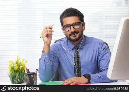 An employee sitting in office with earphones and pencil, smiling.