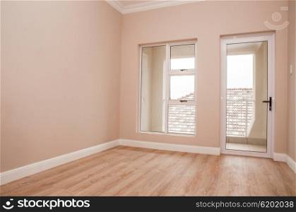 An Empty bedroom of a newly build house with laminated floor and glass windows and door that lead out to the patio.