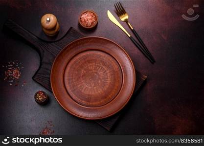 An empty brown ceramic plate on a dark concrete brown background. Preparing the Dinner Table. An empty brown ceramic plate on a dark concrete brown background