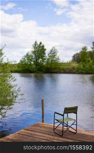 An empty chair and a fishing rod on a wooden pier by the lake. Outdoor recreation. An empty chair and a fishing rod on a wooden pier by the lake. Outdoor recreation.