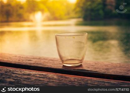 An empty glass on a wooden table by a lake in the afternoon
