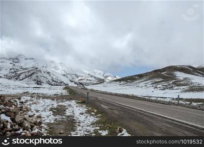 An empty paved road surrounded by snow capped mountains with cloudy sky in the High Atlas range. Morocco.