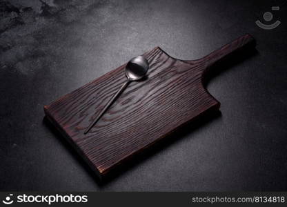 An empty plate with a knife, fork or spoon with a wooden cutting board on a dark concrete background. Preparation of appliances and ingredients for home cooking. An empty plate with a knife, fork or spoon with a wooden cutting board