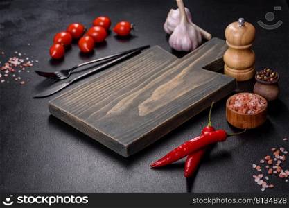 An empty plate with a knife, fork or spoon with a wooden cutting board on a dark concrete background. Preparation of appliances and ingredients for home cooking. An empty plate with a knife, fork or spoon with a wooden cutting board