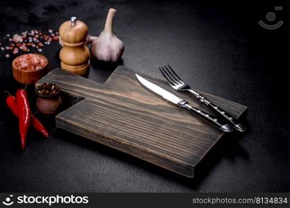 An empty plate with a knife, fork or spoon with a wooden cutting board on a dark concrete background. Preparation of appliances and ingredients for home cooking. An empty plate with a knife, fork or spoon with a wooden cutting board