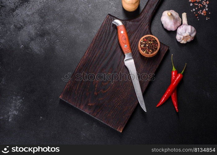 An empty plate with a knife, fork or spoon with a wooden cutting board on a dark concrete background. Preparation of appliances and ingredients for home cooking. An empty plate with a knife, fork or spoon with a wooden cutting board