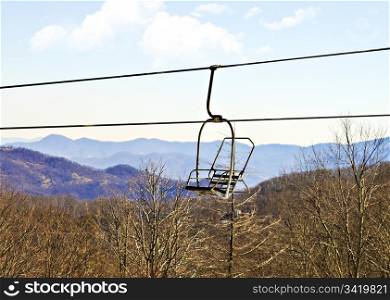 An empty seat on a ski lift with mountains in the background.