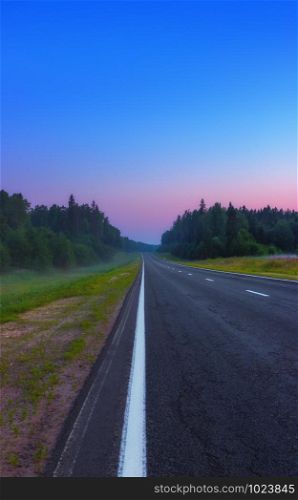 An empty straight asphalt road leads to a pink dawn under the cloudless blue sky in the misty summer morning. Russian federal highway A119. Selective soft focus, space for copy.