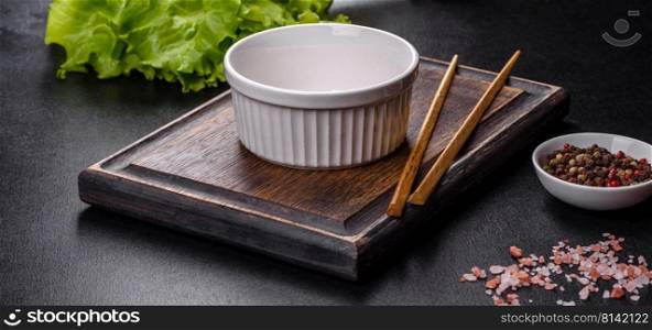 An empty white bowl and sticks on a wooden cutting board on a dark concrete background. Asian food. An empty white bowl and sticks on a wooden cutting board
