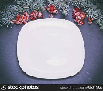 an empty white square plate on a black background, at the top green spruce branches and clusters of red viburnum