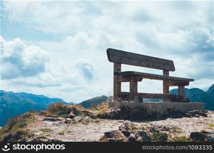 an empty wooden bench at the top of the mountain, overlooking the amazing view on valley and mountain peaks, on a sunny day with clouds. Beautiful breathtaking nature