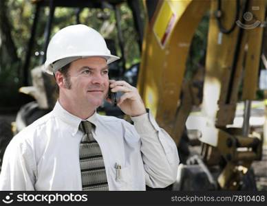 An engineer on a construction site, talking on the phone.