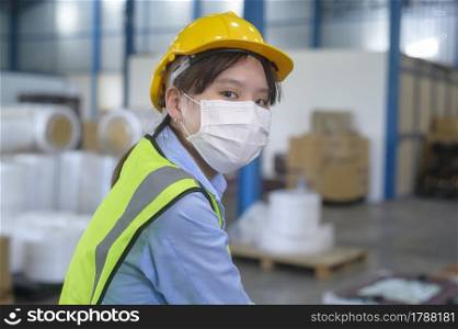 An engineering woman wearing medical mask , protective helmet working in warehouse factory
