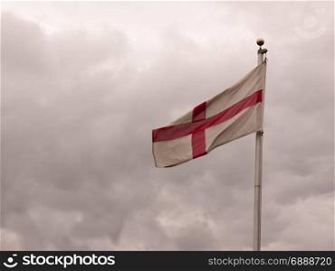 an england flag on a pole swaying in the overcast sky background