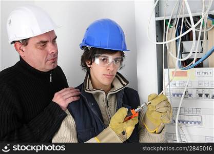 An experienced electrician watching his young apprentice