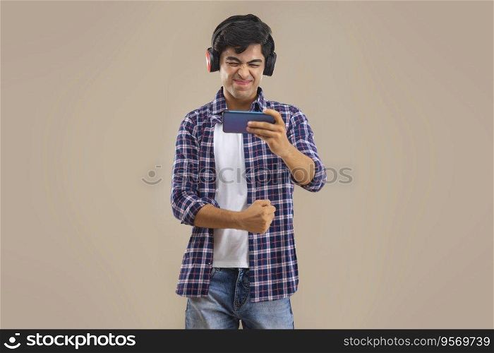 AN EXPRESSIVE TEENAGER HOLDING MOBILE PHONE AND WEARING HEADPHONES