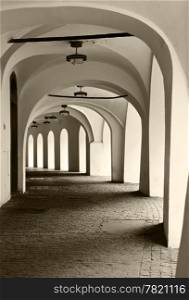 An exterior hallway of a building in Prague. The arches along the exterior highlight the contrast between light and darkness resulting from shadows against the white walls.