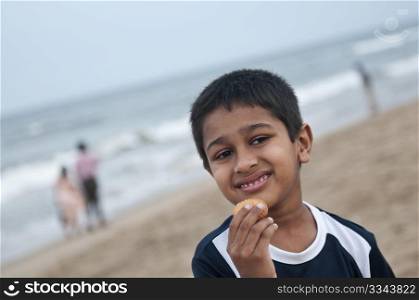 An handsome young Indian boy eating cookies at the beach