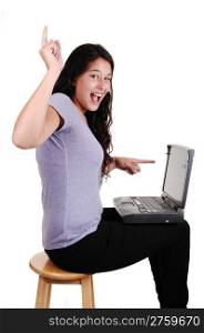 An happy young woman pointing with her finger to her laptop and up inthe air, sitting in black jeans on a chair, for white background.