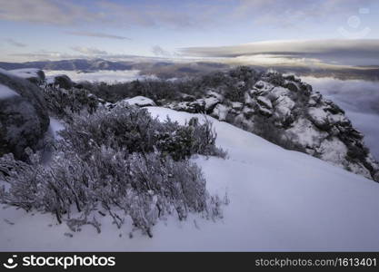 An icy dawn atop Old Rag Mountain in Shenandoah National Park, Virginia as fog swirls in the lower valleys and clouds billow atop Skyline Drive.