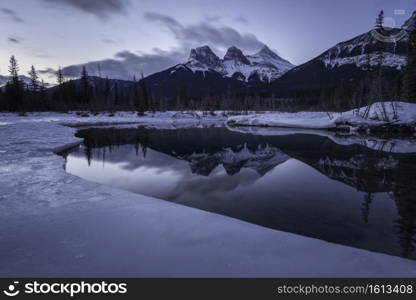 An icy dawn reflection of the Three Sisters in Canmore, Alberta, Canada.