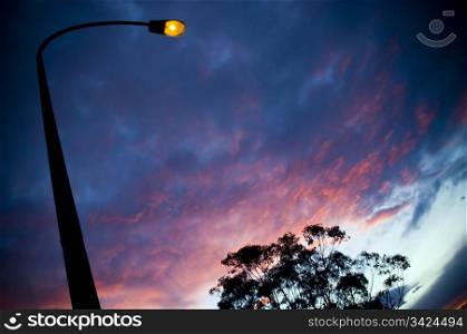 An illuminated street-lamp rises up against sunset / sunrise clouds