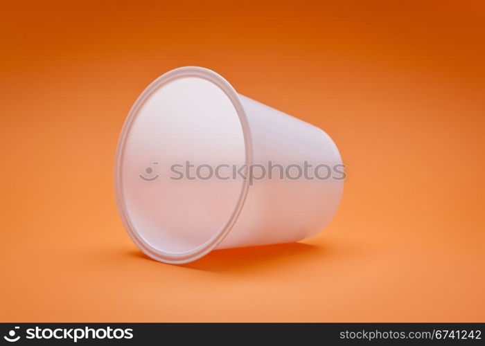 An image of a white empty plastic cup on an orange background