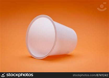 An image of a white empty plastic cup on an orange background