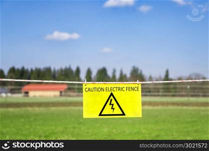 An image of an electric fence at a green meadow warning