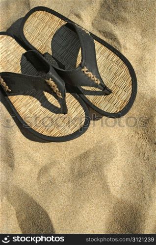 An image of sandals resting on the hot sand of a tropical beach.