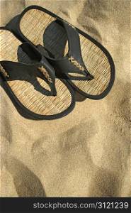 An image of sandals resting on the hot sand of a tropical beach.