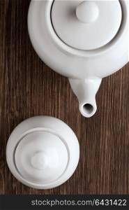 An image of white china tea pot and sugar bowl on wooden table.