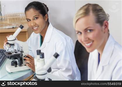 An Indian Asian female medical or scientific researcher or doctor using her microscope in a laboratory with her colleague.