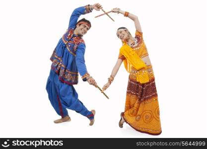An Indian couple in traditional wear performing Dandiya Raas over white background