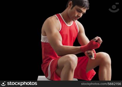 An Indian male boxer taping up hands against black background