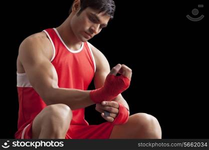 An Indian male boxer taping up hands isolated over black background