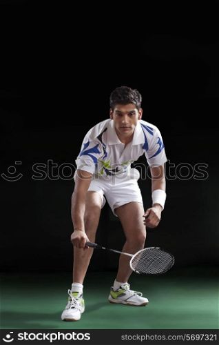 An Indian male player in sportswear playing badminton over black background
