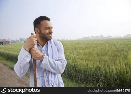 An Indian man looking away while holding a stick