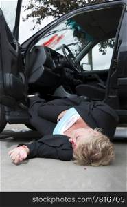 An injured driver with a severe head wound, lies unconsciously on the ground, fallen from her vehicle after an accident