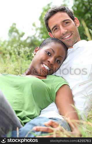 An interracial couple lying on grass.