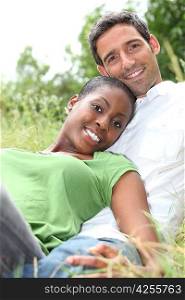 An interracial couple lying on grass.