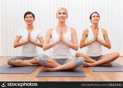 An interracial group of three beautiful young women sitting cross legged in a yoga position at a gym