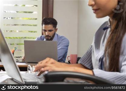 AN OFFICE EXECUTIVE SERIOUSLY WORKING AND A COLLEAGUE SITTING IN FRONT OF HIM