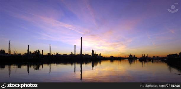An oil refinary at sunset, situated in an industrial harbor area, with its piers, jetties and mooring buoys.