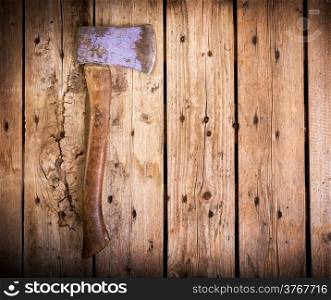 An old axe with a wooden handle and wear marks sits on a rough timber background