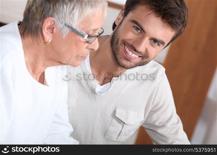 An old bespectacled lady seated near a smiling young man.