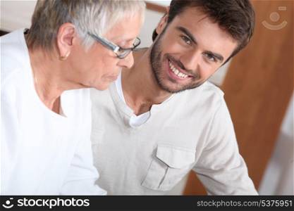 An old bespectacled lady seated near a smiling young man.